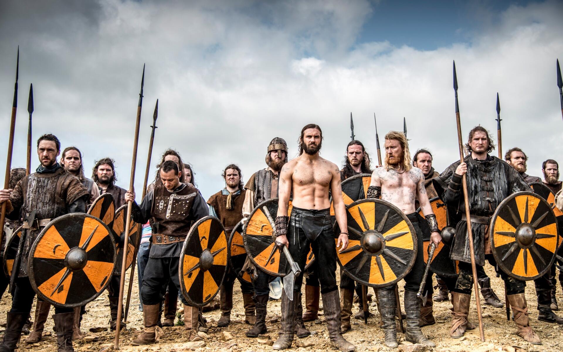 HD PC desktop wallpaper featuring a fierce group of warriors from Vikings (2013) standing ready with shields and spears under a cloudy sky.