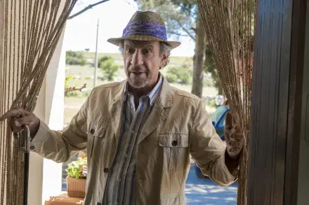 A scene from the TV show The White Lotus featuring F. Murray Abraham, standing at a doorway, framed by curtains and greenery, capturing a moment of intrigue and character.