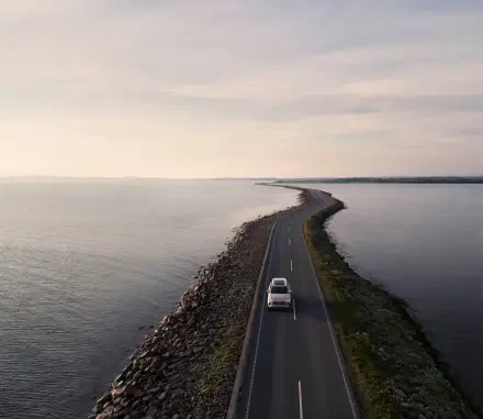 A Volvo XC90 Facelift drives along a scenic coastal road, bordered by water, captured in a stunning 4K Ultra HD wallpaper.
