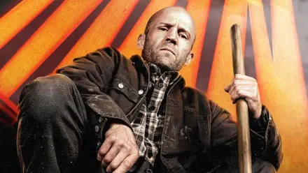 Jason Statham portrays a determined character in A Working Man, set against a striking backdrop with bold orange rays, captured in this vivid 4K Ultra HD wallpaper.