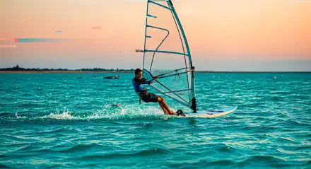 A windsurfer glides across the ocean at sunset, captured in vivid 4K Ultra HD, showcasing dynamic water sports action against a serene sky.