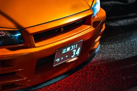 Close-up of an orange Nissan Skyline GT-R R34 front end with illuminated headlights and Japanese license plate, captured in 4K Ultra HD for a PC desktop wallpaper.