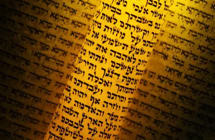 HD desktop wallpaper showing close-up of Hebrew Torah verses on parchment, warm golden light highlighting Jewish Bible text and religious script for a textured background.