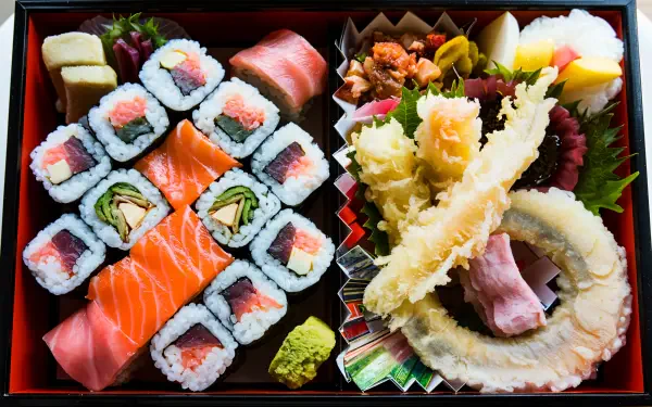 A beautifully arranged bento box featuring sushi rolls, sashimi, and tempura, captured in stunning 4K Ultra HD, making it an appealing desktop wallpaper and background.