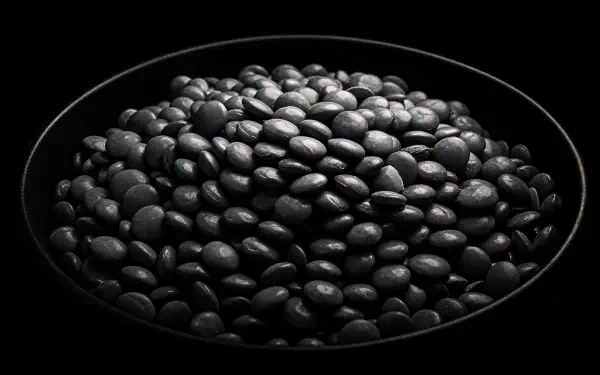A close-up of a pile of black lentils in a dark plate, set against a black background, showcasing texture and detail. This striking image serves as a 4K Ultra HD PC desktop wallpaper.