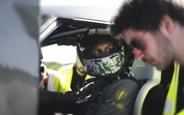 A car racer in a helmet sits in a sleek vehicle, engaging with a teammate in sunglasses. An 8K Ultra HD wallpaper showcasing the thrill of motorsport.