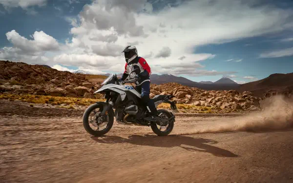 A BMW R1300GS motorcycle navigates a rugged dirt path, capturing a thrilling moment in motocross against a backdrop of dramatic clouds and mountains. 4K Ultra HD quality.
