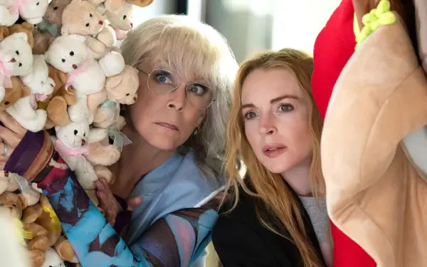 Jamie Lee Curtis and Lindsay Lohan peeking from behind a wall of stuffed animals in a scene from the movie Freakier Friday. This image serves as a vibrant 4K Ultra HD wallpaper.