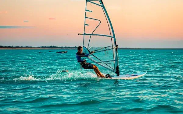 A windsurfer skillfully navigates the vibrant turquoise waters against a sunset backdrop, creating a dynamic scene perfect for a 4K Ultra HD desktop wallpaper.