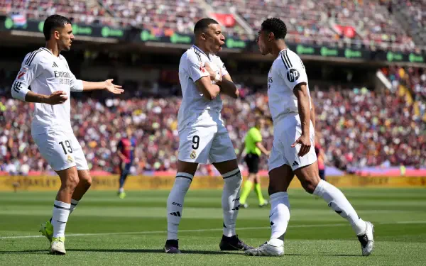Real Madrid players Kylian Mbappé and Jude Bellingham celebrate on the field during a vibrant soccer match in this 4K Ultra HD wallpaper.