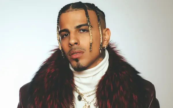 HD desktop wallpaper featuring Puerto Rican music artist Rauw Alejandro in a stylish fur coat and layered necklaces against a plain background.