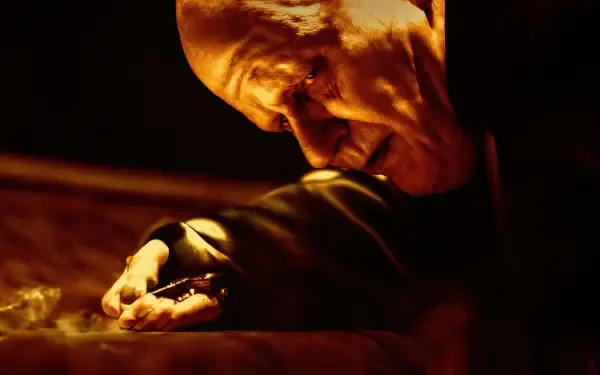 Dune: Part Two 4K Ultra HD PC desktop wallpaper — close-up of a gaunt, robed figure in orange light, clutching a small object over a table, dramatic shadows and textured detail.