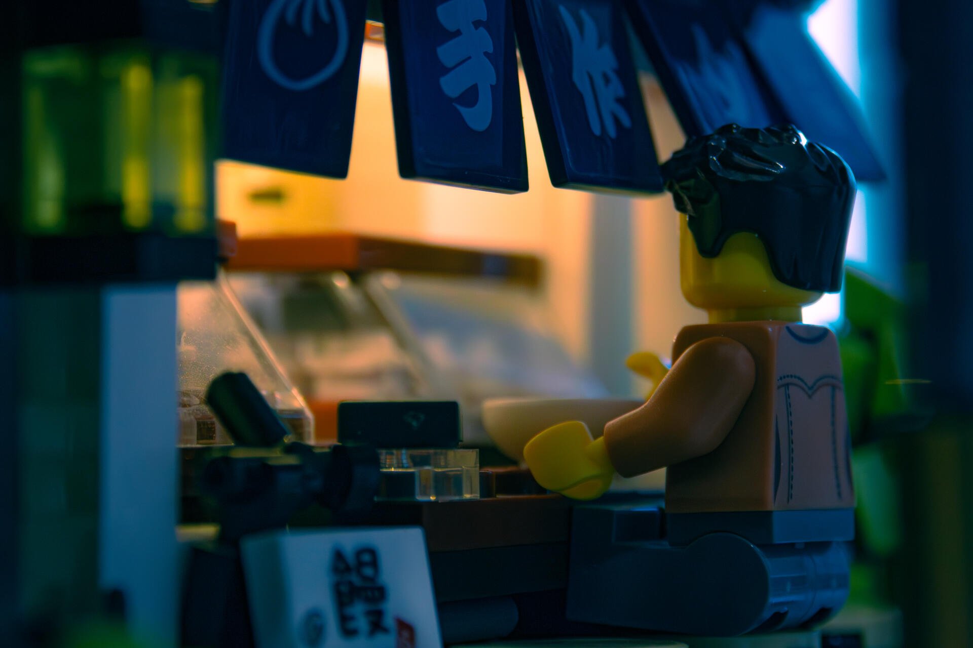 4K Ultra HD PC desktop wallpaper showing a man made LEGO figurine seated at a dimly lit counter, bathed in moody blue-green neon light.