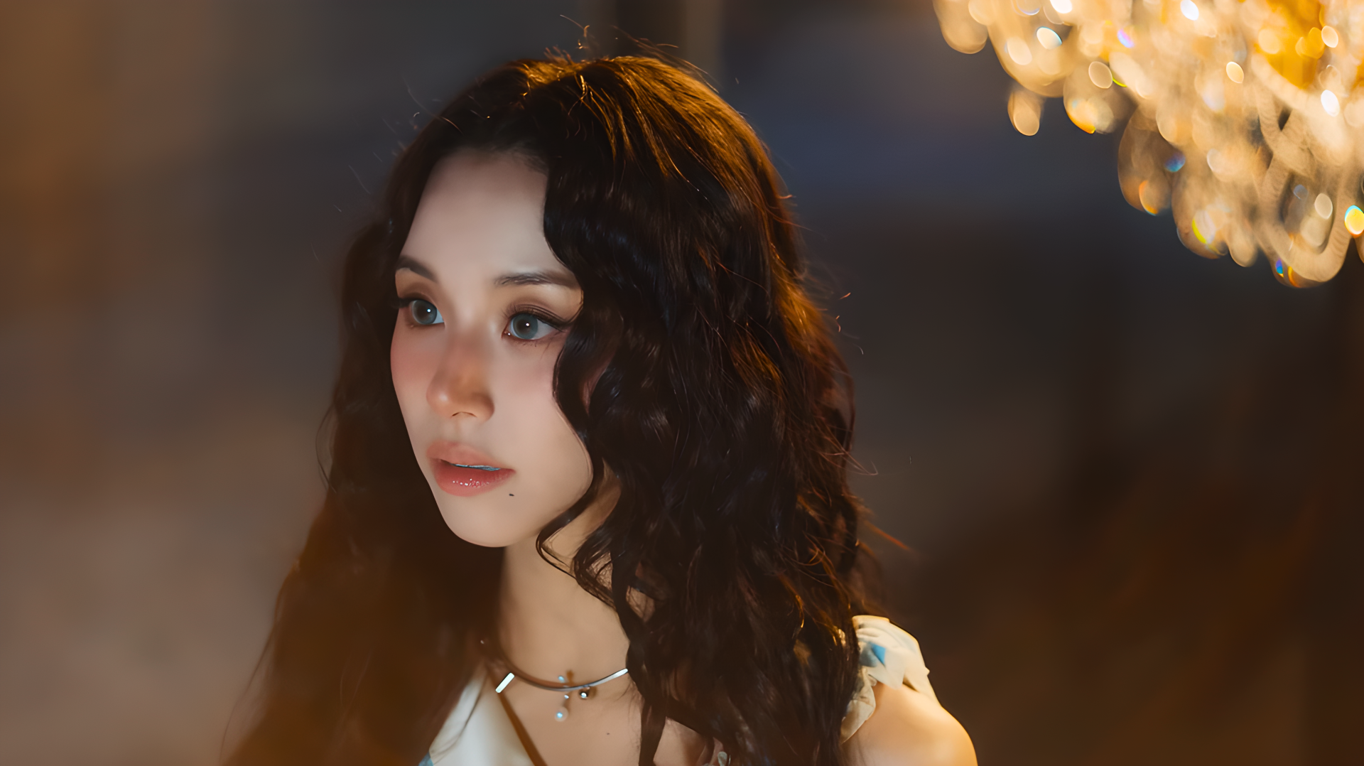 Close-up portrait of a doll-like model with dark curly hair and soft makeup, bathed in warm chandelier light — 4K Ultra HD PC desktop wallpaper.