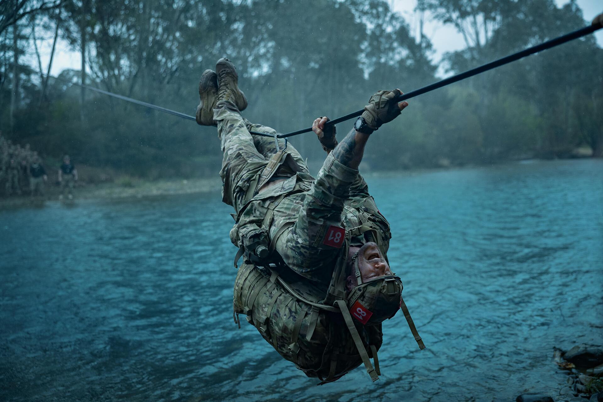 Movie still, War Machine (2026): soldier in military training crosses a rope over a lake, dramatic 5K Ultra HD PC desktop wallpaper background.