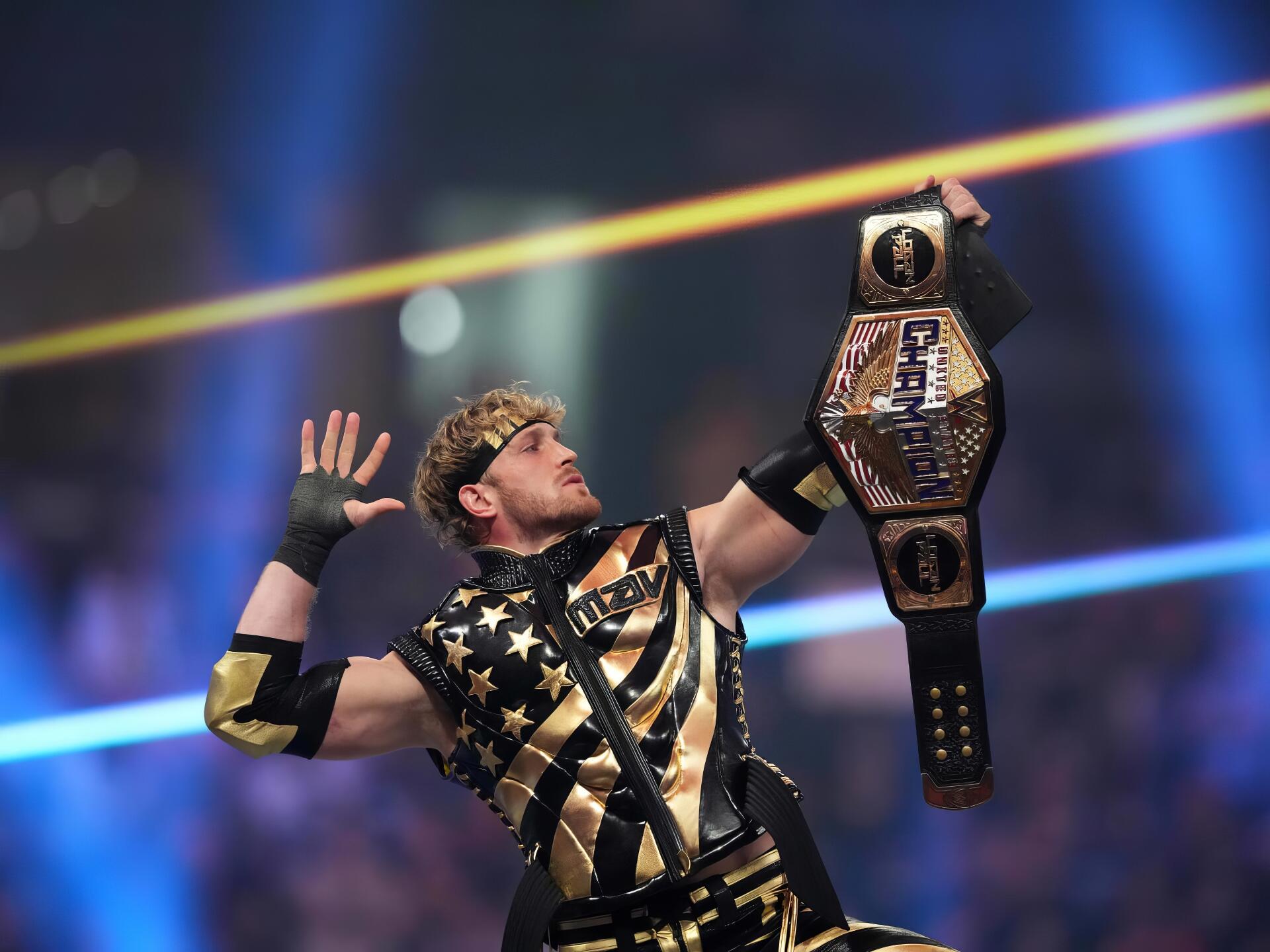 HD PC desktop wallpaper of a celebrity WWE champion raising a championship belt, wearing black-and-gold ring gear and posing triumphantly under arena lights.