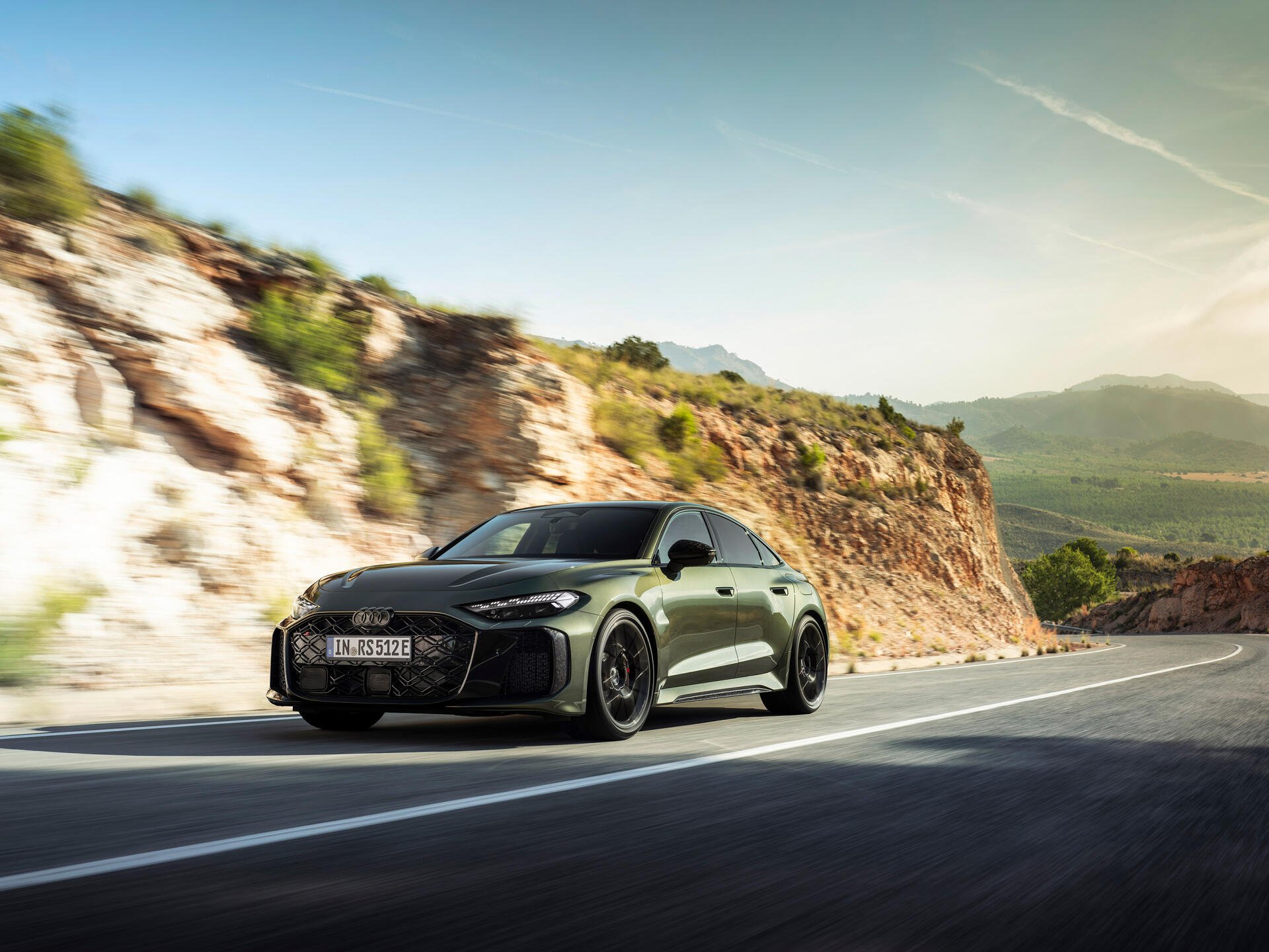 Audi RS5 driving on a sunlit winding mountain road with rocky cliffs and distant valley; 2K Quad HD PC desktop wallpaper/background.