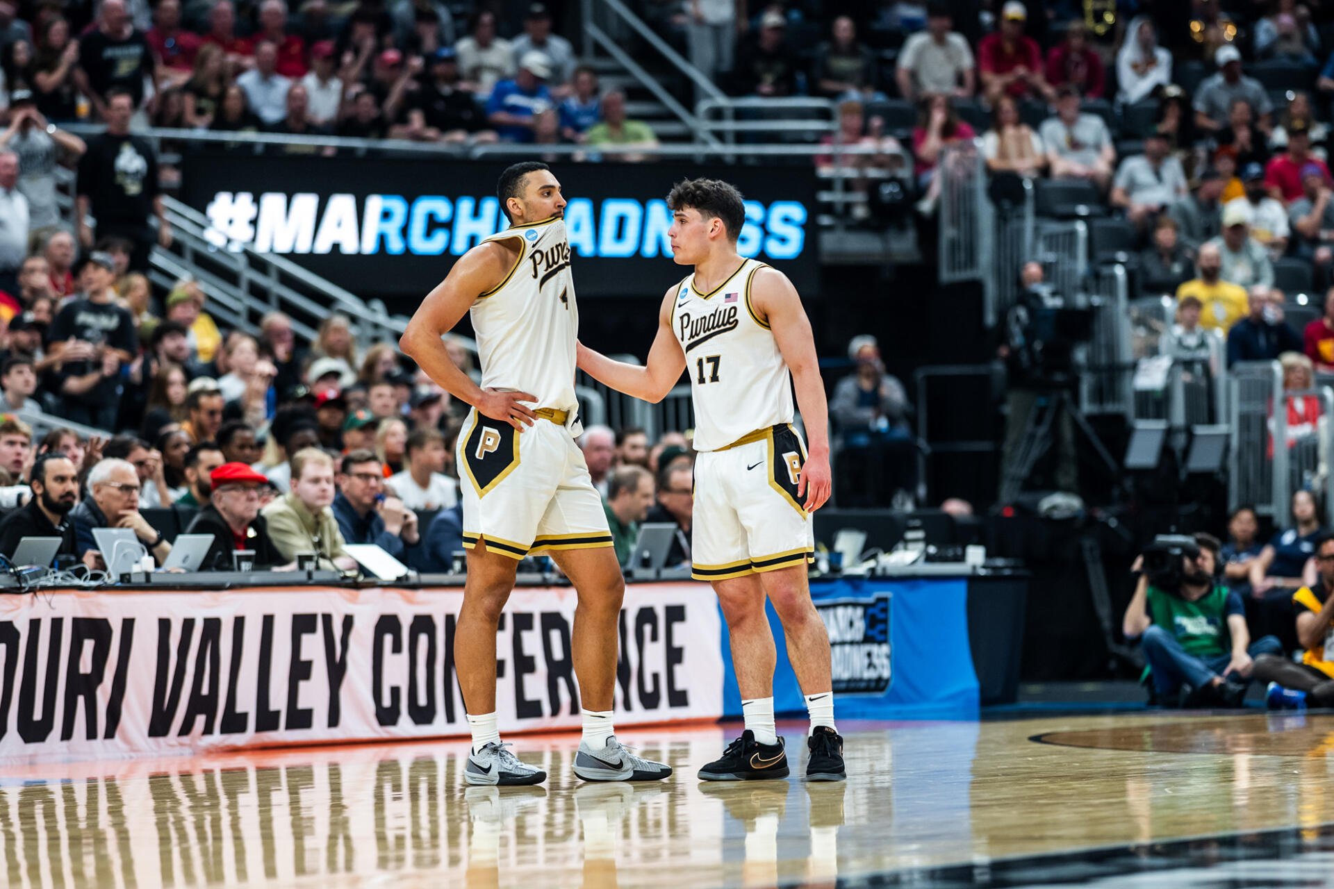 HD PC desktop wallpaper/background showing two NCAA Purdue Boilermakers basketball players conversing on-court amid a packed arena during a March Madness game.