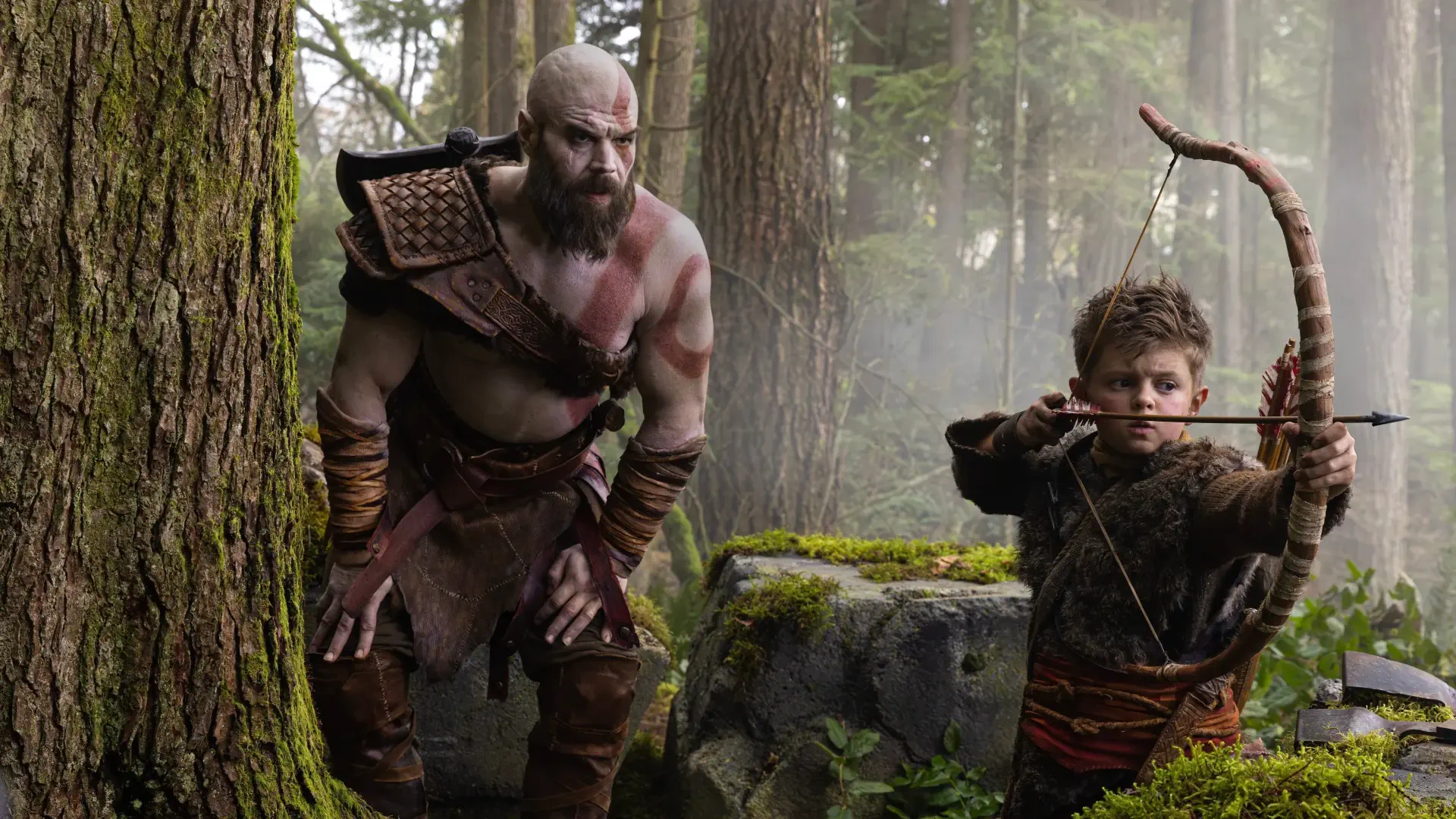 God of War (TV Show) 2K Quad HD PC desktop wallpaper — rugged bearded warrior and young archer practicing in a misty, moss-covered forest.