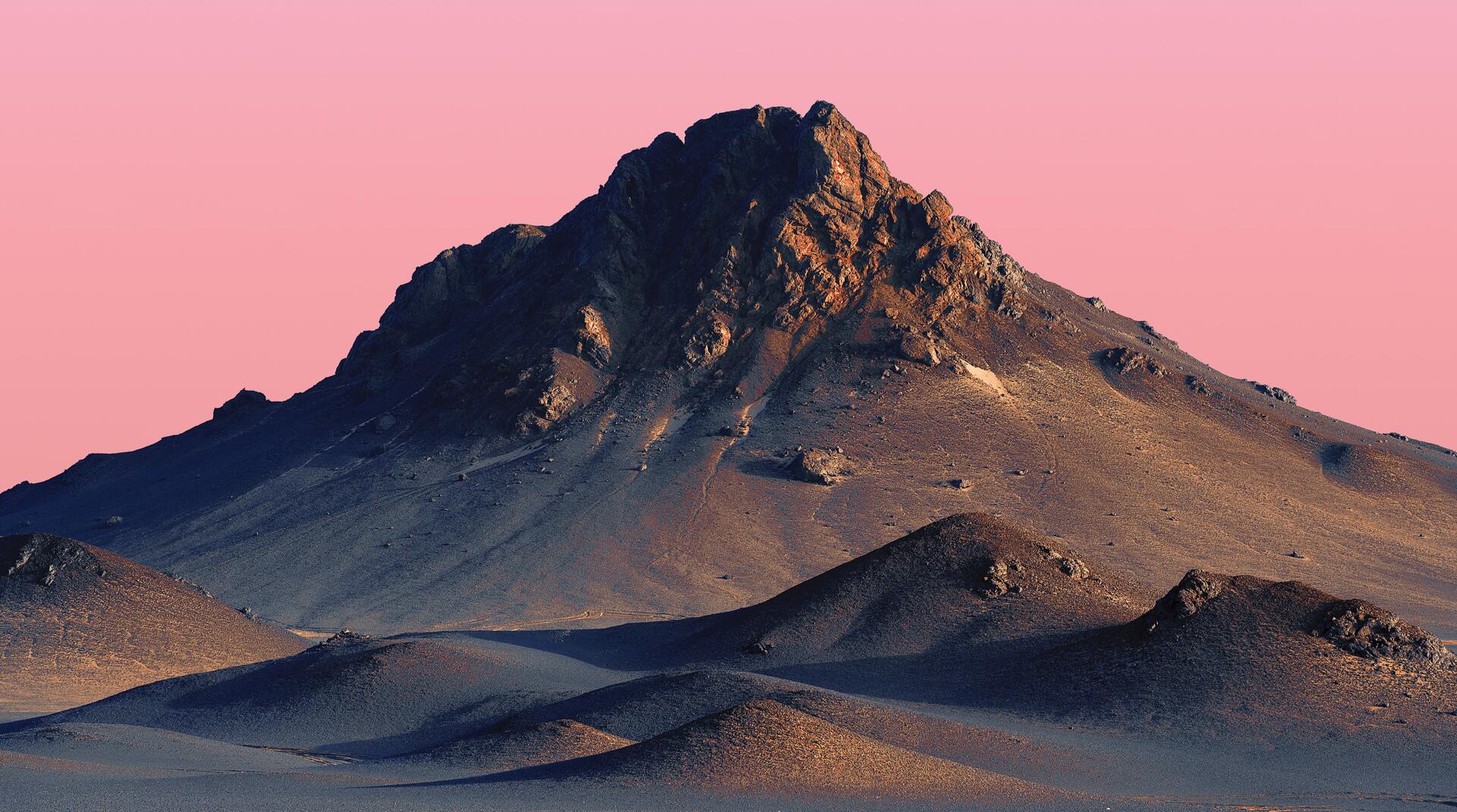 2K Quad HD PC desktop wallpaper: solitary desert mountain peak rising from rippled dunes beneath a soft pink sky.