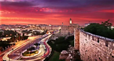 HD PC desktop wallpaper: panoramic city view of Jerusalem at sunset, man-made ancient stone walls beside winding traffic light trails.