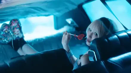Blonde woman in a neon-blue car backseat, holding a heart-shaped lollipop and gazing at the camera, K-pop–style 4K UHD PC desktop wallpaper.