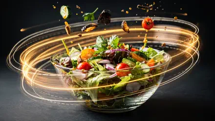 Glass bowl of mixed salad with cherry tomatoes, greens and herbs, ingredients suspended in swirling golden light trails on a dark backdrop. 4K Ultra HD PC wallpaper.