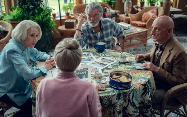 4K Ultra HD PC desktop wallpaper: scene from the movie The Thursday Murder Club — four older friends gathered around a floral table strewn with photos and clues in a cozy lounge.