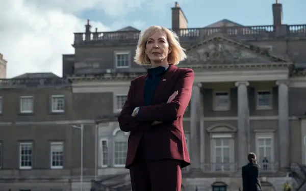 2K Quad HD desktop wallpaper: promotional image for TV show The Diplomat — a confident older actress in a burgundy suit stands with arms crossed before a stately government building.