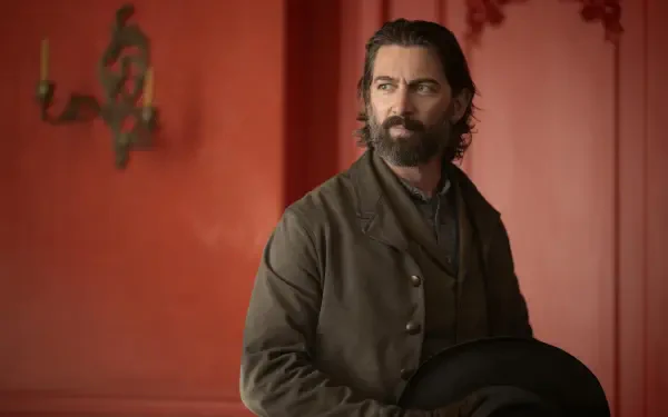 Bearded man in a period coat holding a hat against a red wall, still from TV show The Abandons — 2K Quad HD PC desktop wallpaper/background.