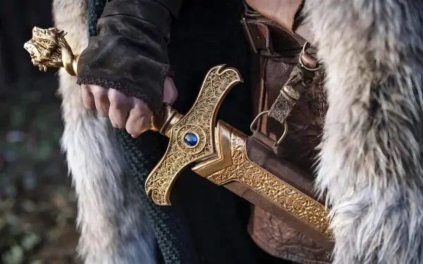 Close-up of a cloaked figure gripping an ornate golden sword with a blue gem — HD PC desktop wallpaper/background for the TV show The Pendragon Cycle: Rise of the Merlin.