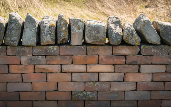 Brick wall topped with weathered stones and a grassy bank, 4K Ultra HD PC desktop wallpaper and background.