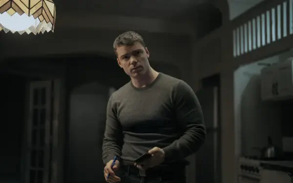 Thriller 2K Quad HD PC wallpaper: brooding man in a dim, shadowed kitchen holding a notebook, tense moody lighting evoking The Night Agent.