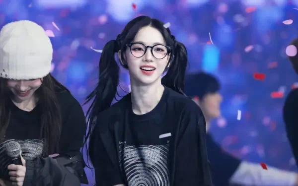 4K Ultra HD desktop wallpaper of a smiling K-pop singer in glasses and pigtails onstage, wearing a black tee as confetti falls against vibrant, blurred concert lights.