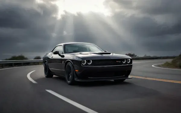 Black Dodge Challenger hugging a curved road beneath dramatic sunlight rays — 2K Quad HD PC desktop wallpaper and background.