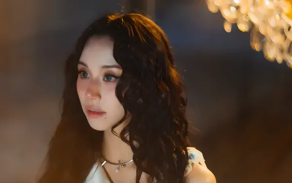 Close-up portrait of a doll-like model with dark curly hair and soft makeup, bathed in warm chandelier light — 4K Ultra HD PC desktop wallpaper.