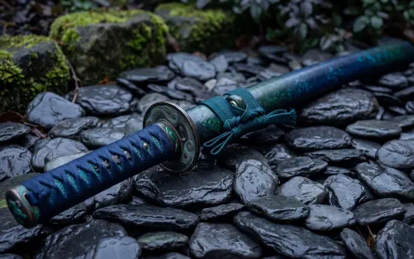 5K Ultra HD PC desktop wallpaper and background: a teal‑handled ninja sword rests on wet black stones with moss and shadowed foliage.