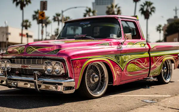 Lowrider truck in vibrant pink and green with ornate pinstriping and chrome rims parked by palm trees — 4K Ultra HD PC desktop wallpaper and background.