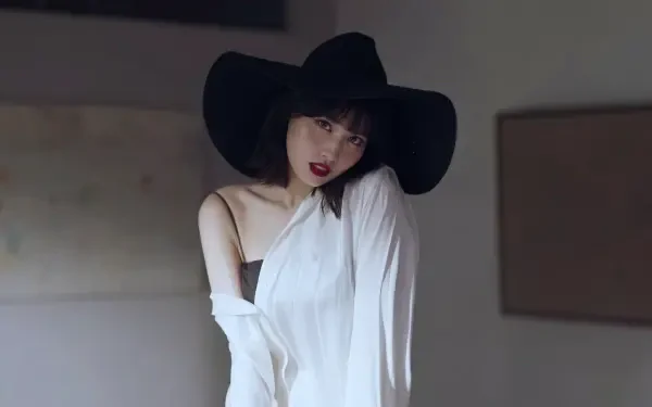 Woman in a wide-brim black hat and white off-shoulder top, gazing toward the camera in a softly lit interior — 5K Ultra HD desktop wallpaper.