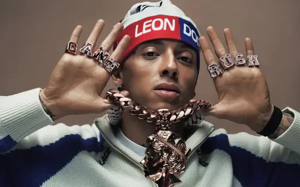 HD PC desktop wallpaper of a person wearing a red-white-blue headband reading LEON, heavy chain pendant and lettered rings, hands raised toward the camera against a beige background.