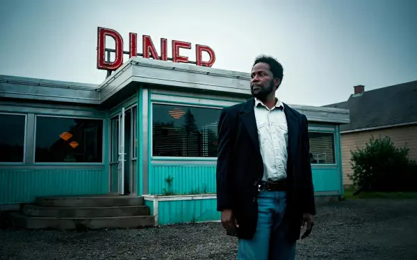 HD PC desktop wallpaper/background from TV show From (2022): a suited man stands before a turquoise roadside diner beneath a moody, overcast sky.