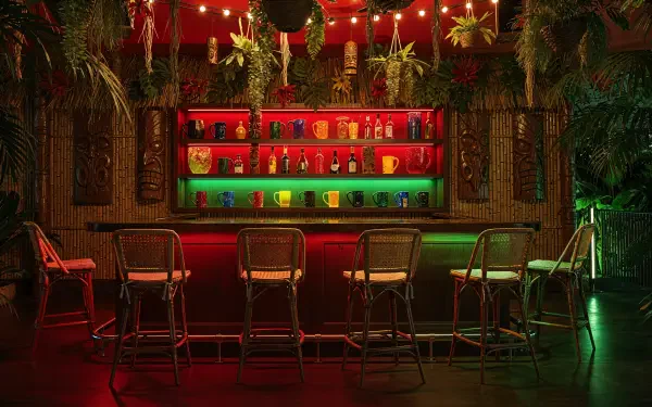 Tiki bar interior with rattan stools, colorful backlit bottles, hanging plants and string lights — 4K Ultra HD PC desktop wallpaper and background.