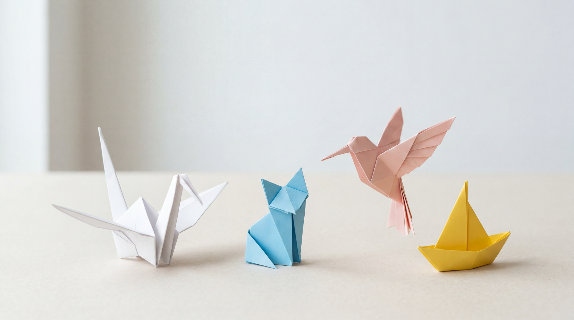 Clean 5K Ultra HD PC desktop wallpaper and background showing a minimal beige surface with four origami figures: white crane, blue folded animal, pink hummingbird, yellow paper boat.