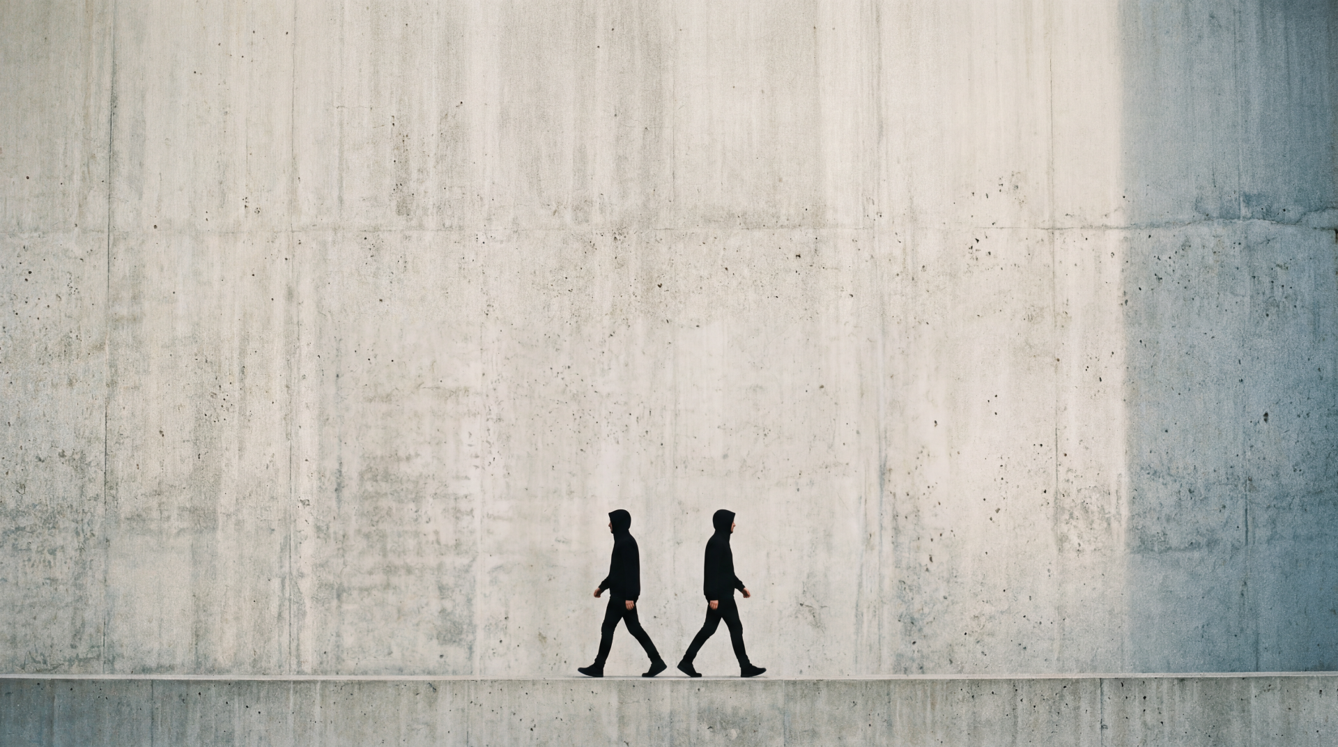 Minimal 5K Ultra HD PC Desktop Wallpaper and Background — two walking silhouettes cross a long, textured concrete wall under soft, neutral light.
