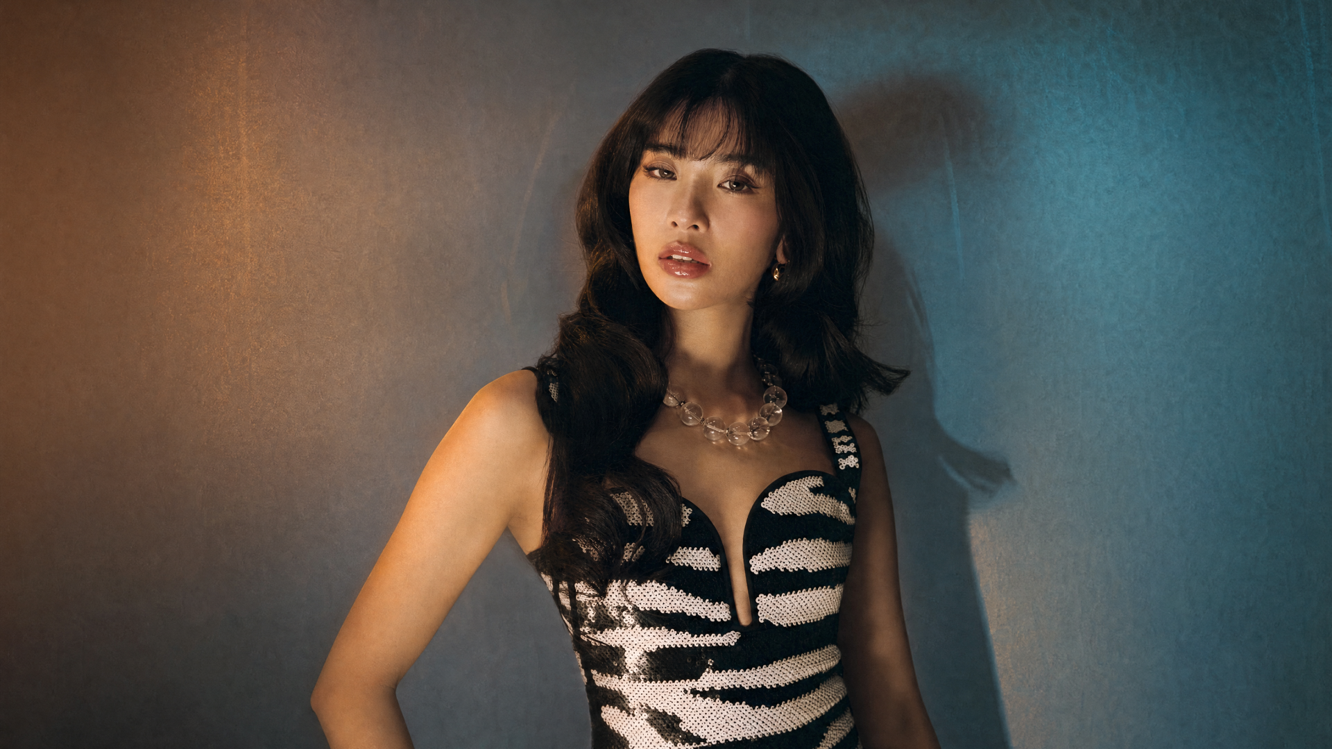 Katseye 4K Ultra HD PC desktop wallpaper: dark-haired woman in a zebra-print dress with layered necklaces, moody teal and amber lighting and a confident pose.