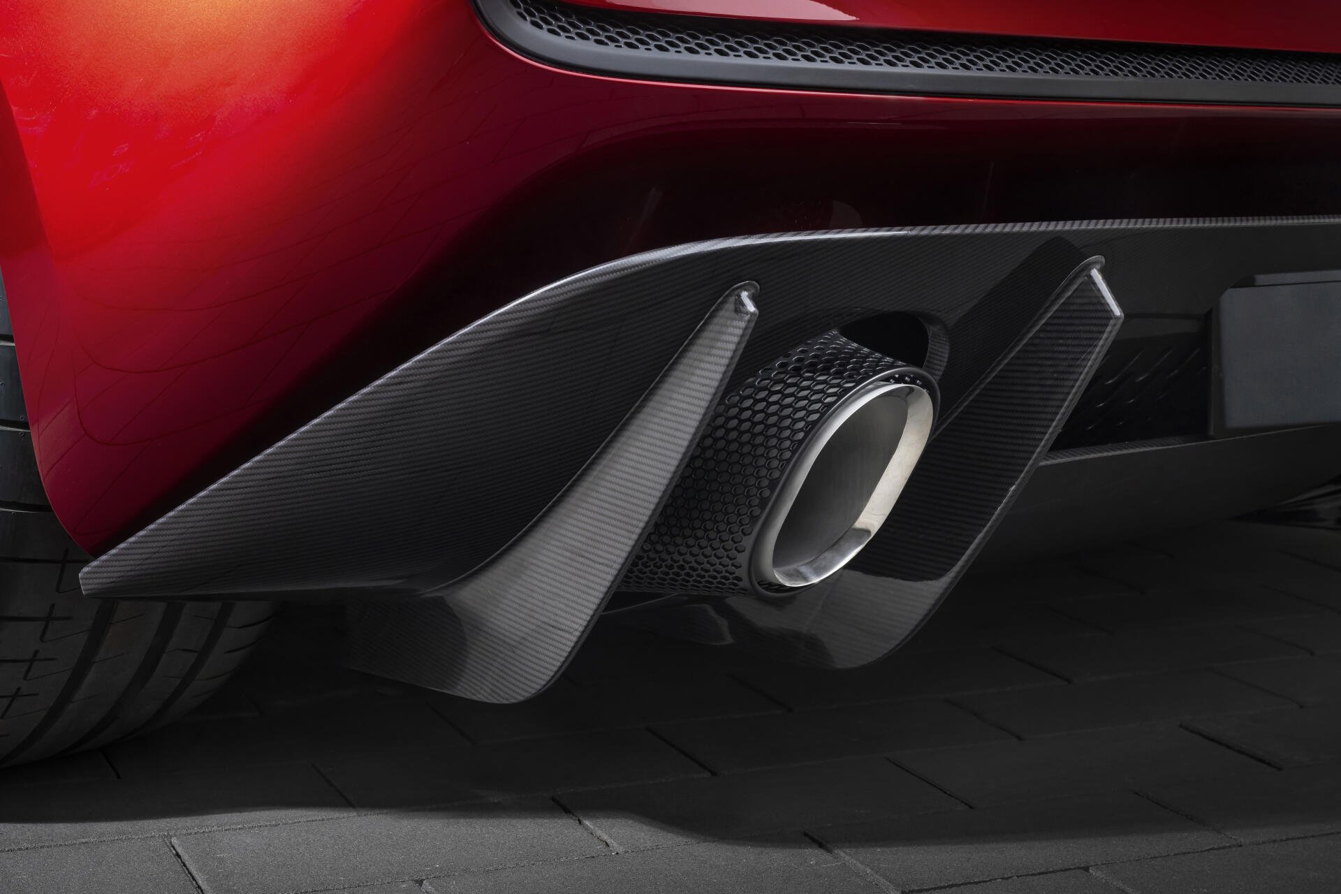 Close-up of a red McLaren McL 6GT rear bumper with carbon-fiber diffuser and chrome exhaust tailpipe, 8K Ultra HD PC desktop wallpaper background.