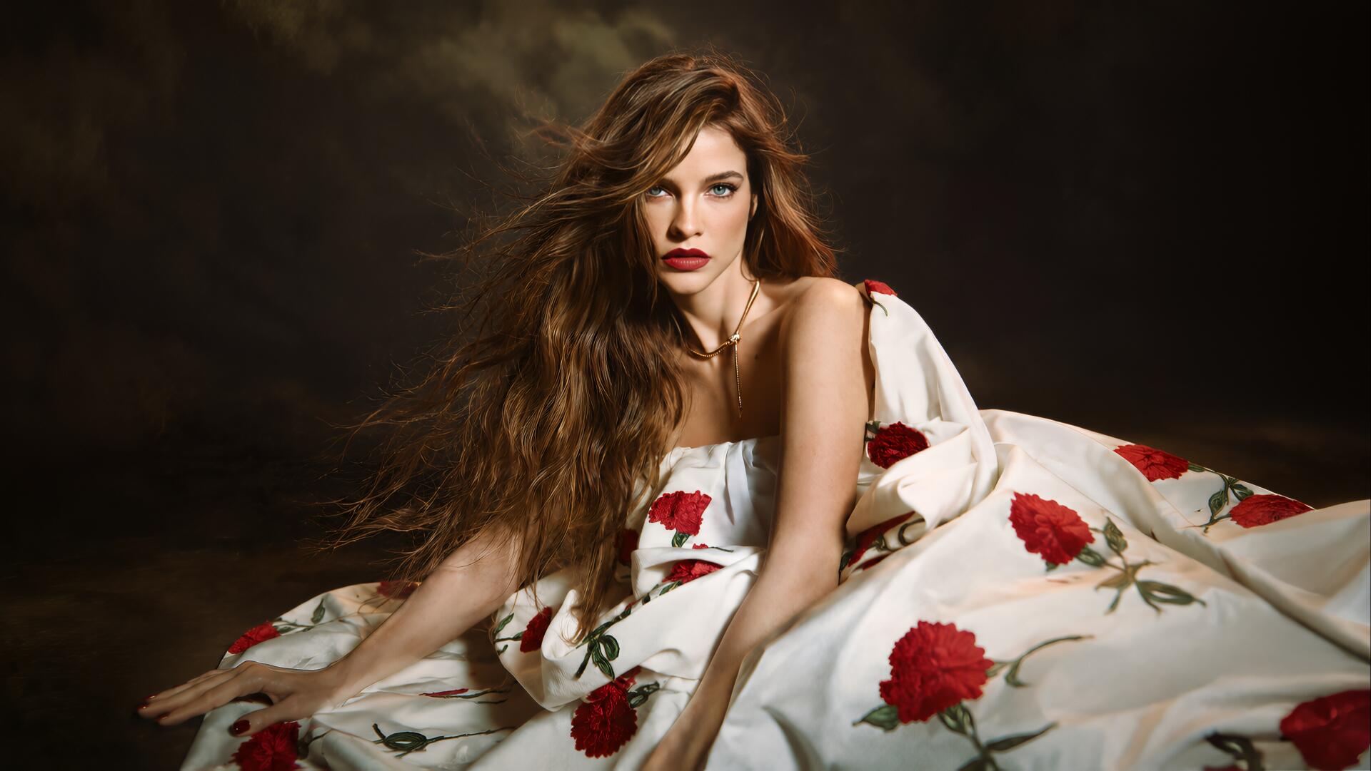 Celebrity model in a white gown patterned with red roses, long wavy hair and red lips reclining against a dark backdrop — 4K Ultra HD PC desktop wallpaper.