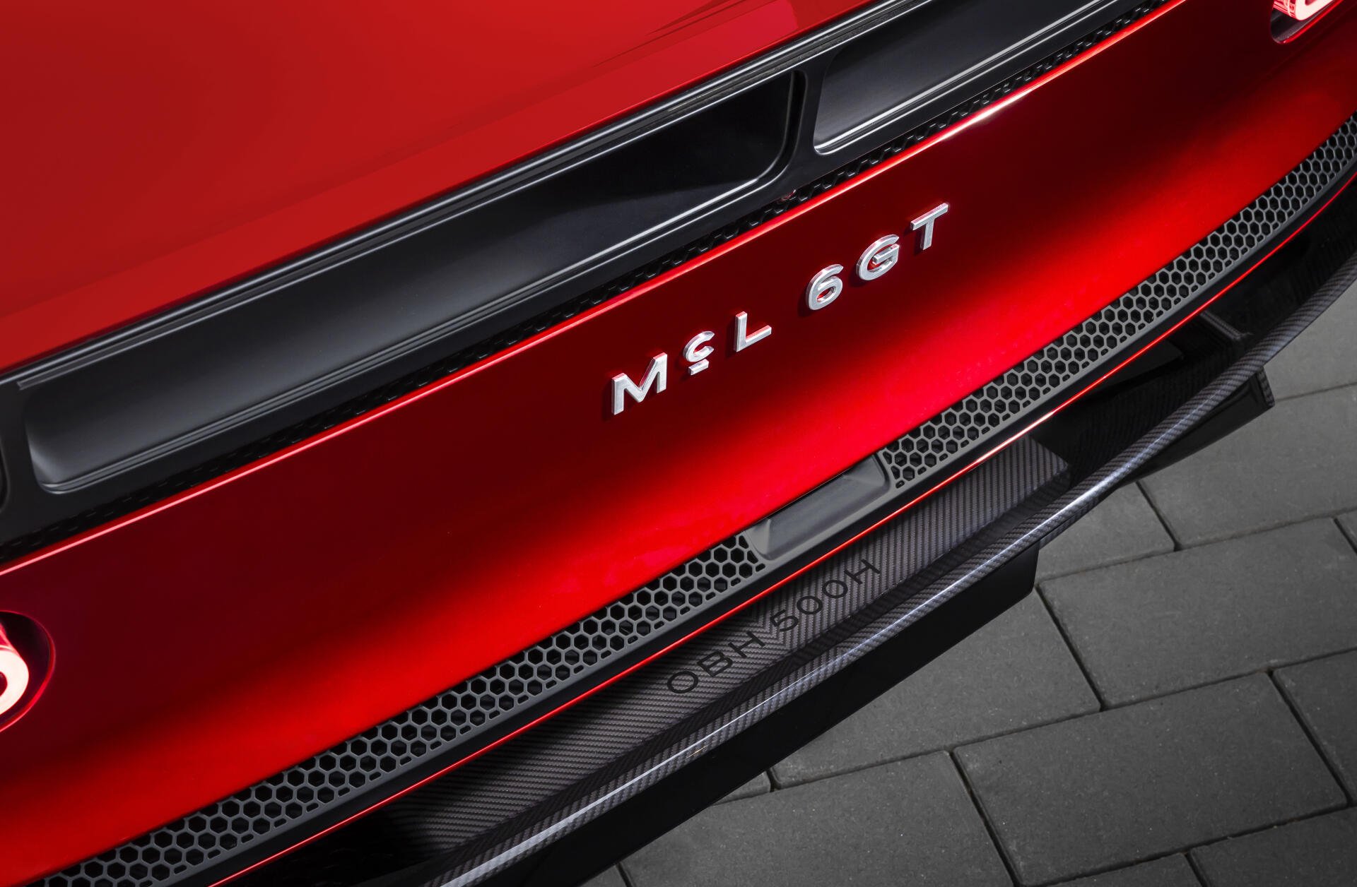 Close-up of red McLaren McL 6GT sports car rear bumper and badge, showing carbon trim and grille details — 5K Ultra HD PC desktop wallpaper background.