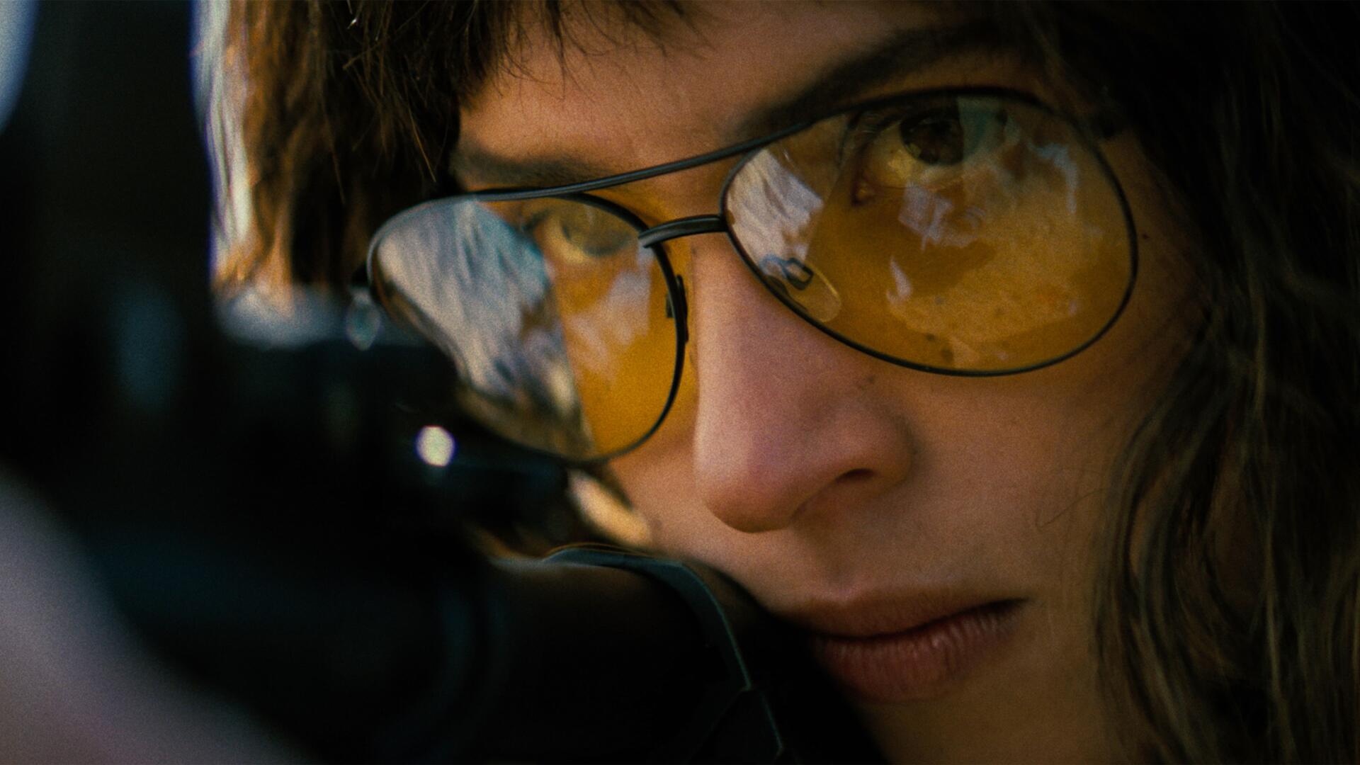 Close-up portrait of a female actor wearing yellow-tinted glasses, intense, focused gaze in a cinematic Onslaught style — 4K Ultra HD PC desktop wallpaper/background.