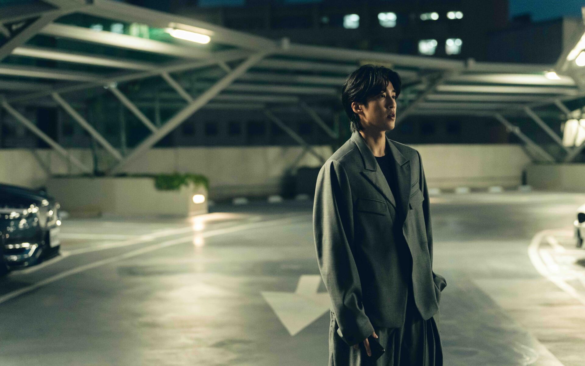8K Ultra HD PC desktop wallpaper: lone man from The Fixers stands in a dim, cinematic parking garage with dramatic lighting and empty lanes.